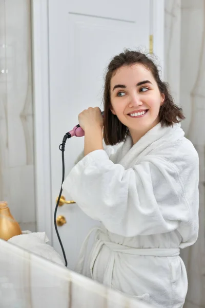 Frau benutzt Haarglätter im Badezimmer. — Stockfoto