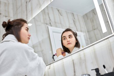 Tuvalette saç düzleştirici kullanan bir kadın..