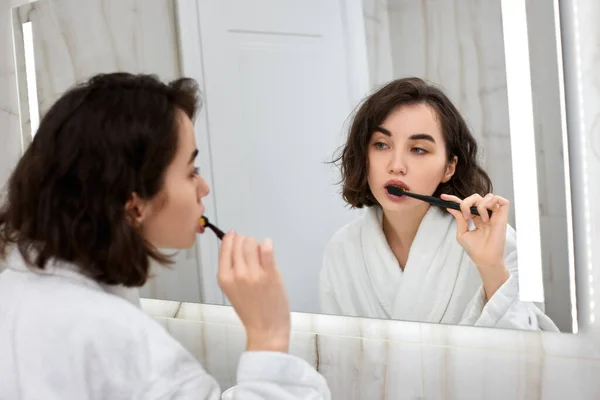 Nő fehér fürdőköpenyben fogmosás előtt tükör — Stock Fotó