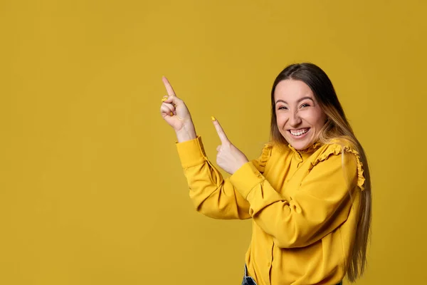 Молода жінка вказує на жовтий фон — стокове фото