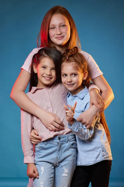 Trois enfants filles debout ensemble sur fond bleu — Photo