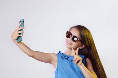 Akıllı telefondan selfie çekerken zafer işareti gösteren kız çocuğu