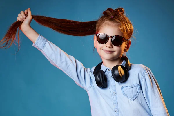 Rudowłosa dziewczynka w okularach przeciwsłonecznych i słuchawkach bezprzewodowych — Zdjęcie stockowe