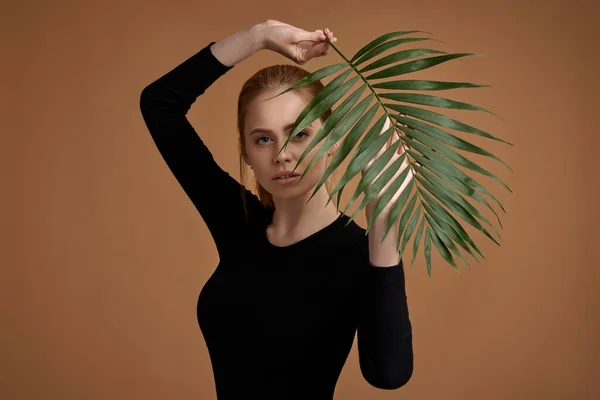 Blonde woman holding exotic leaves near her face — Fotografie, imagine de stoc