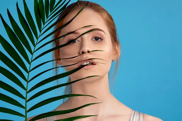 Blonde woman hiding behind palm tropical leaves — Fotografie, imagine de stoc