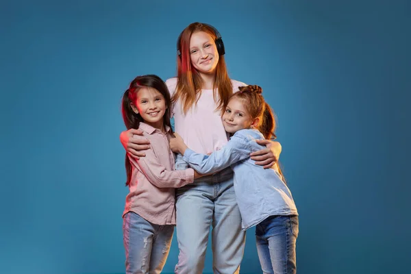 Trois enfants filles debout ensemble sur fond bleu — Photo