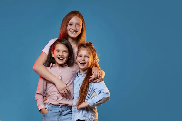 Trois enfants filles debout ensemble sur fond bleu — Photo