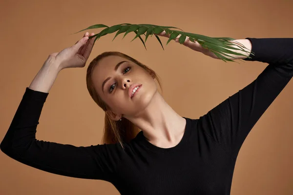 Blonde woman holding exotic leaves near her face — Fotografie, imagine de stoc
