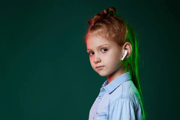 Счастливая рыжеволосая девочка в наушниках слушает музыку на бежевом фоне — стоковое фото