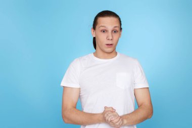 Mavi arka planda izole edilmiş tişörtlü üzgün genç adam..