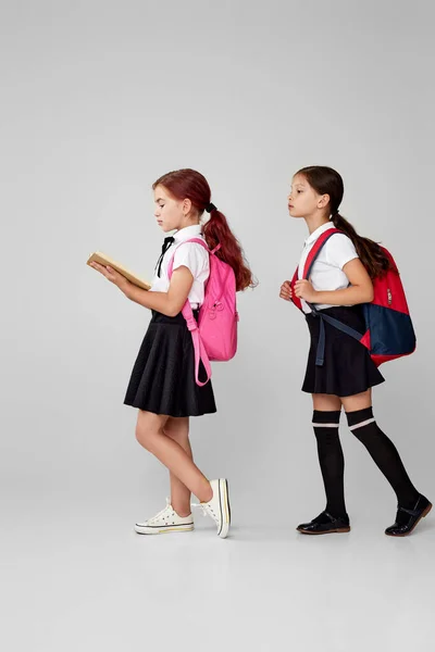 Two little cheerful friends schoolgirls with backpacks read book — Stock Photo, Image