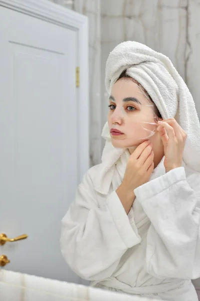 Vrouw in wit badjas in de voorkant van spiegel in badkamer — Stockfoto