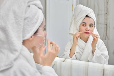 Banyoda aynanın önünde beyaz bornozlu bir kadın.