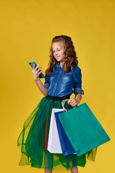 어린 소녀는 쇼핑백을 들고 스마트폰을 사용 한다 — 스톡 사진