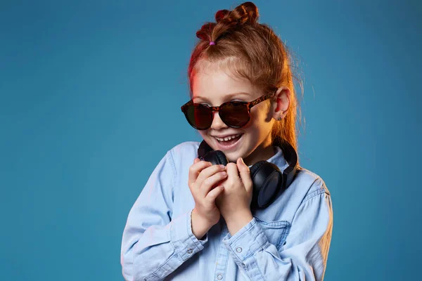 Rudowłosa dziewczynka w okularach przeciwsłonecznych i słuchawkach bezprzewodowych — Zdjęcie stockowe