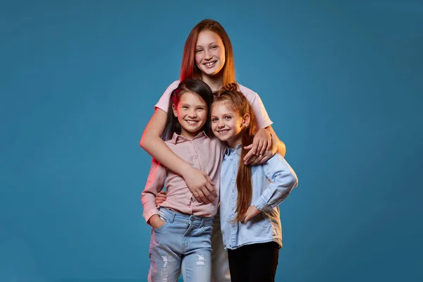 Drie kids meisjes staan samen op blauwe achtergrond — Stockfoto