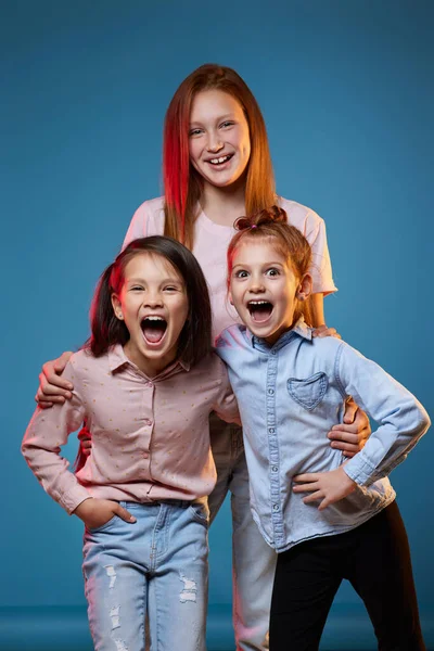 Trois enfants filles debout ensemble sur fond bleu — Photo