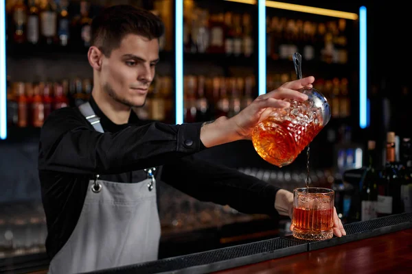 Barman in apron pours old fashioned cocktail into glass — Stock Photo, Image