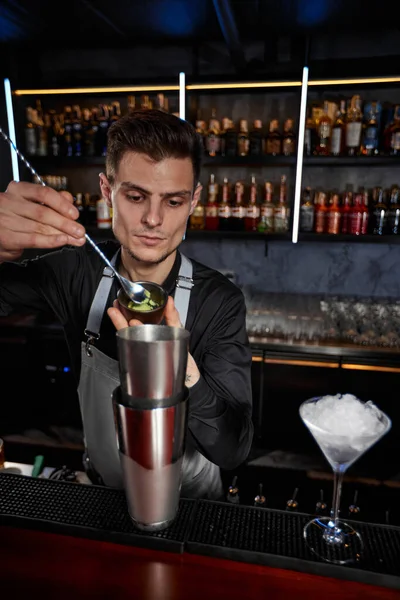 Bartender em avental adiciona ingrediente ao shaker — Fotografia de Stock