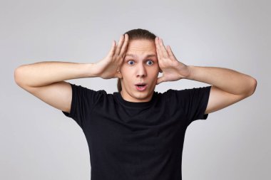 Gri arka planda izole genç yakışıklı adam şaşırdı.