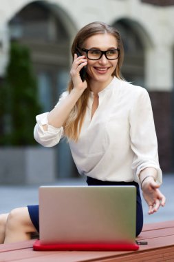 Bilgisayarda çalışan akıllı telefonlu bir iş kadını.