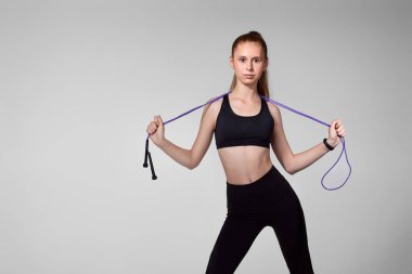 Siyah spor giysili güzel bir kadın ip atlıyor.