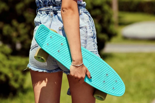 Gadis muda bercelana pendek memegang skateboard biru — Stok Foto