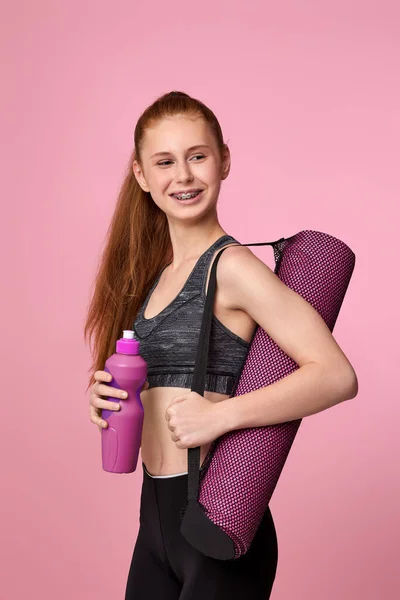 Mulher em sportswear segurando garrafa de água e tapete de fitness — Fotografia de Stock