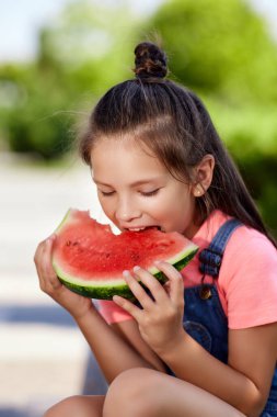 Çocuk kız güneşli bir günde karpuz yiyor.
