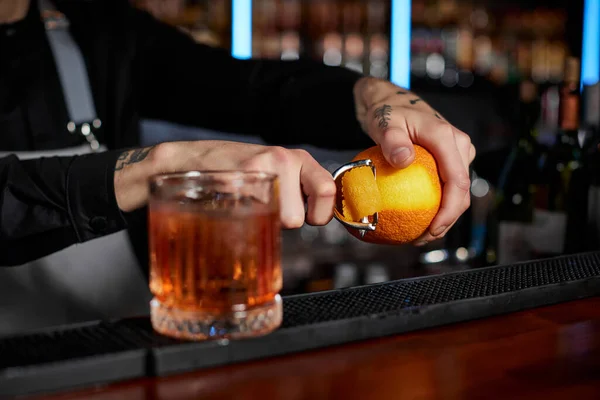 Camarero hace un cóctel en una copa con cáscara de naranja —  Fotos de Stock