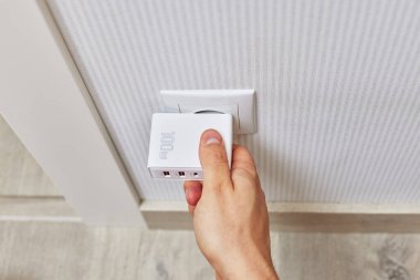 male hand insert a plug of the phone charger into socket at home