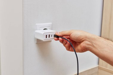 male hand insert a plug of the phone charger into socket at home