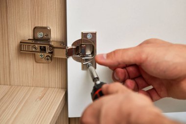 Repairman assembling cabinet and screwing door hinge at home, close-up
