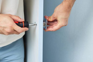 worker installing new handle of cabinet door with screwdriver, close-up. furniture assembly service