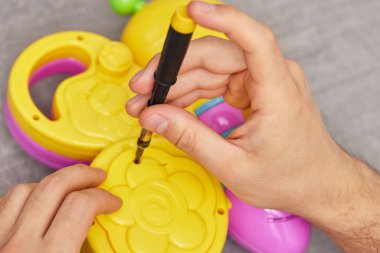 male hands with screwdriver repairing kids toy on grey table. repair shop