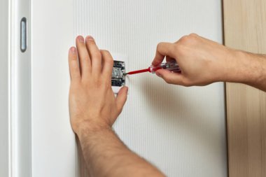 electrician working on light switch using screwdriver inside, close-up