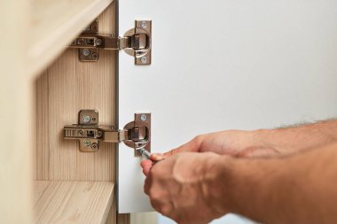 handyman installing cabinet and screwing door hinge at home, close-up