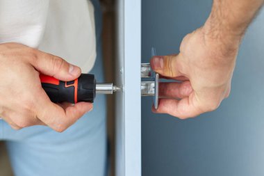 worker installing new handle of cabinet door with screwdriver, close-up. furniture assembly service