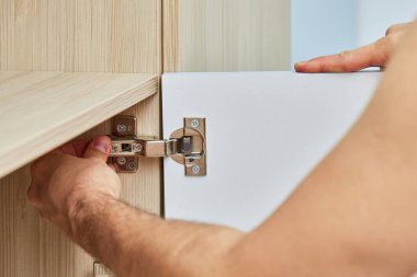 handyman assembling cabinet and screwing door hinge , close-up