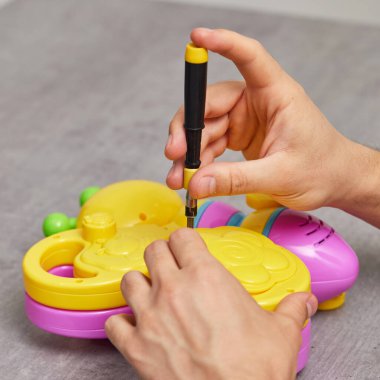 male hands with screwdriver repairing kids toy on grey table. repair shop