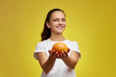 Mutlu beyaz kadın, sarı arka planda greyfurt tutuyor.