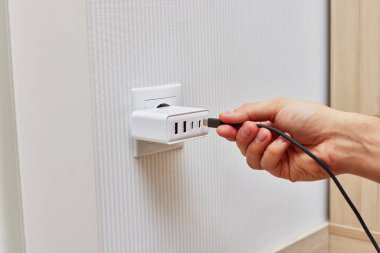 Kadın eli, şarj aletinin fişini evdeki prize takıyor.