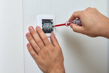 electrician repairing domestic light switch using screwdriver at home, close-up
