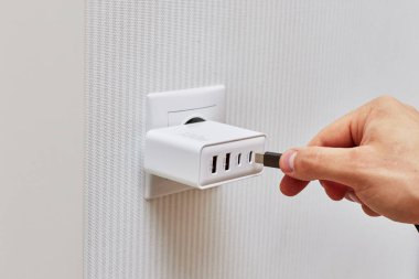 male hand insert a plug of the phone charger into socket at home