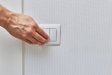 Erkek parmağı mavi duvardaki beyaz ışık düğmesini açıp kapatıyor. Boşluğu kopyala.