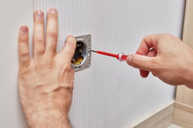 male hands installing electrical wall outlets with a screwdriver at home