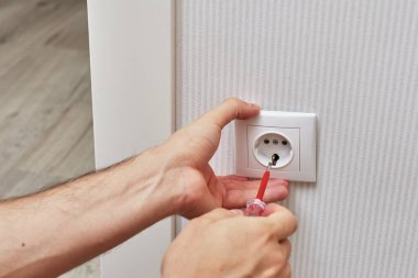 male hands installing electrical wall outlets with a screwdriver at home