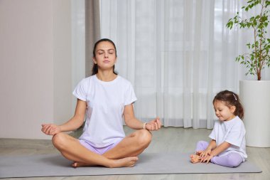 Anne ve kızı evde yoga minderlerinde poz veriyorlar.