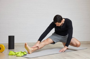 Genç bir adam evdeki yoga minderinde kaslarını geriyor, spor yapıyor.