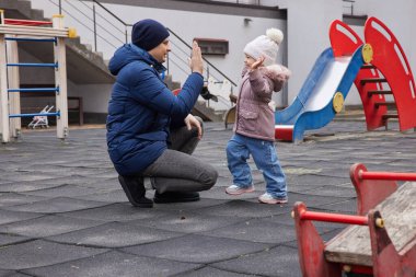 Baba ve kızı oyun parkında beşlik çakıyor, dışarıda neşeli bir anı paylaşıyorlar.